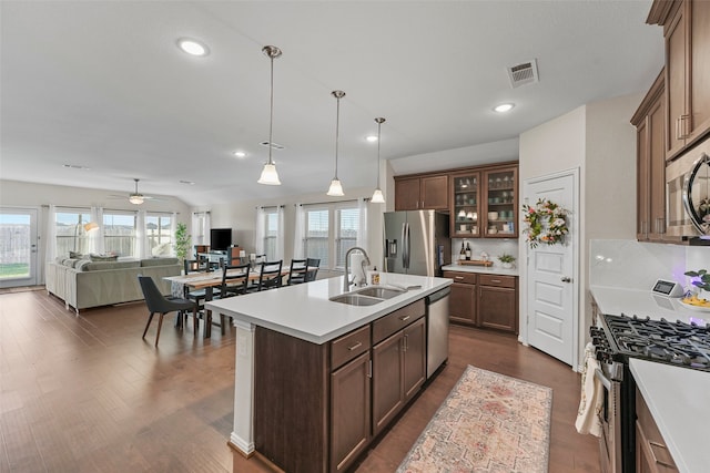 kitchen with dark wood-type flooring, sink, decorative light fixtures, a center island with sink, and appliances with stainless steel finishes