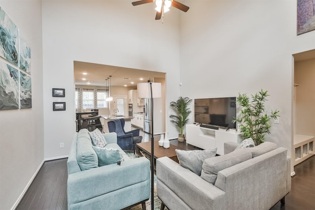 living room featuring dark hardwood / wood-style flooring, ceiling fan, and a high ceiling