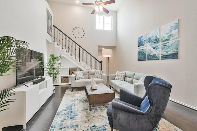 living room featuring dark hardwood / wood-style floors, ceiling fan, and a towering ceiling