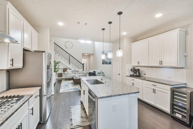 kitchen with beverage cooler, a kitchen island with sink, sink, and white cabinets