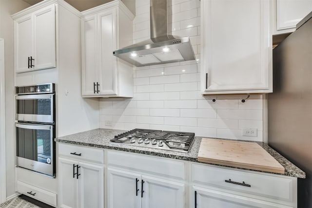 kitchen featuring tasteful backsplash, white cabinets, stainless steel appliances, and wall chimney exhaust hood