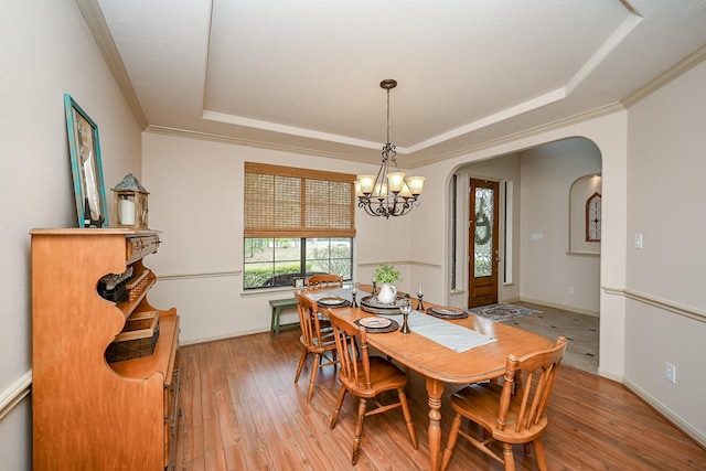 dining room featuring ornamental molding, a notable chandelier, light wood-type flooring, and a tray ceiling