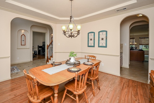 dining area with a raised ceiling, a chandelier, and light wood-type flooring