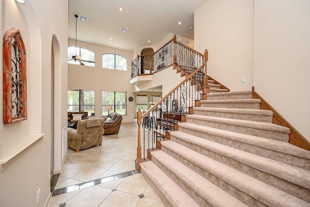 stairs with a towering ceiling, tile patterned floors, and ceiling fan