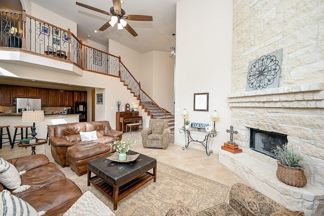 living room featuring a towering ceiling, a fireplace, ceiling fan, and light tile patterned flooring