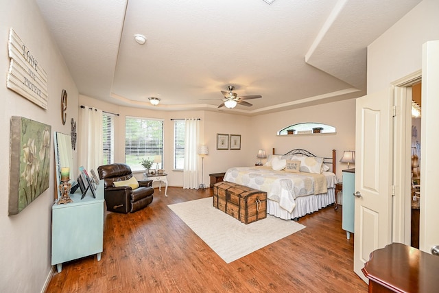 bedroom featuring ceiling fan, dark hardwood / wood-style flooring, a raised ceiling, and a textured ceiling