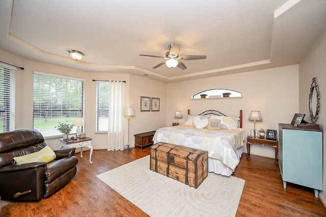 bedroom featuring ceiling fan, dark hardwood / wood-style flooring, a raised ceiling, and a textured ceiling