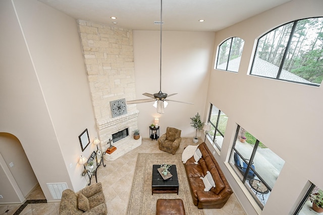 living room with a stone fireplace, ceiling fan, and a high ceiling