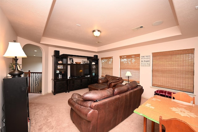 living room with a tray ceiling, light carpet, and a textured ceiling