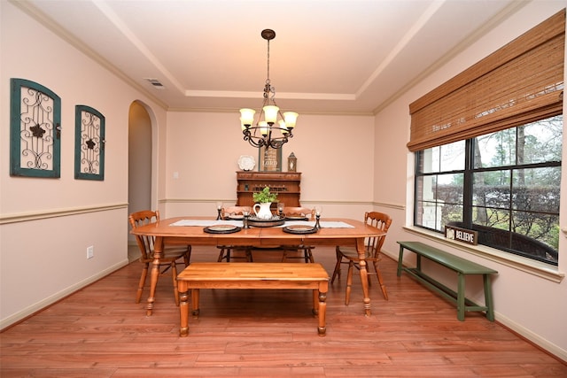 dining area featuring an inviting chandelier, a raised ceiling, and light wood-type flooring