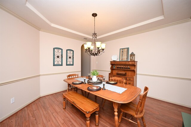 dining room featuring hardwood / wood-style flooring, a tray ceiling, an inviting chandelier, and crown molding