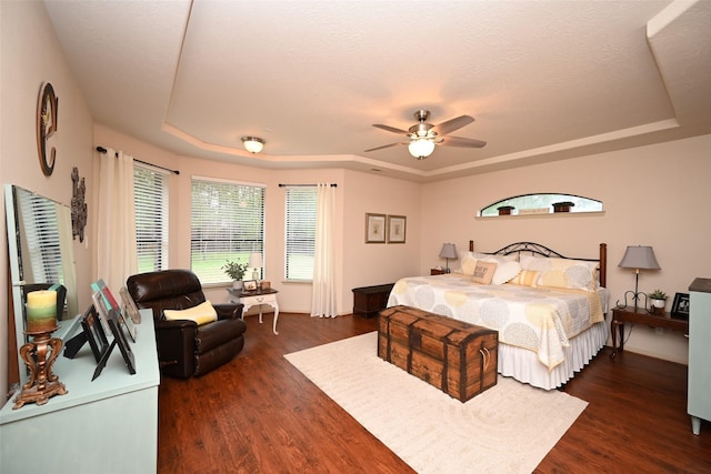 bedroom featuring ceiling fan, dark hardwood / wood-style floors, a raised ceiling, and a textured ceiling