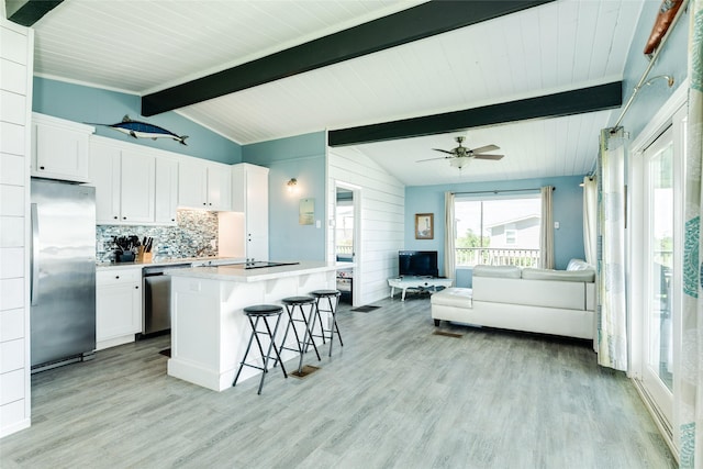 kitchen featuring open floor plan, appliances with stainless steel finishes, white cabinets, and vaulted ceiling with beams