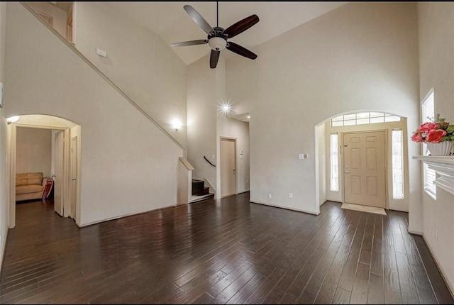 unfurnished living room with dark wood-type flooring, ceiling fan, and a towering ceiling