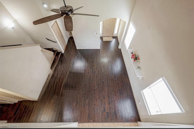 unfurnished living room with dark wood-type flooring, ceiling fan, and a high ceiling