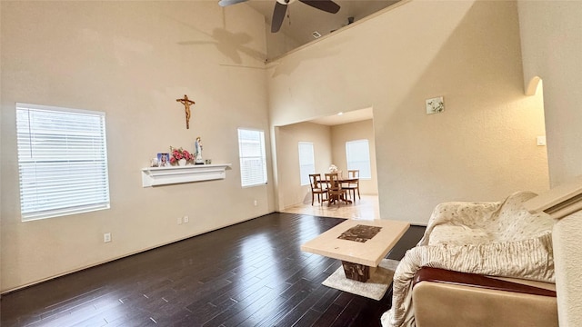 living room with dark wood-type flooring, ceiling fan, and a towering ceiling