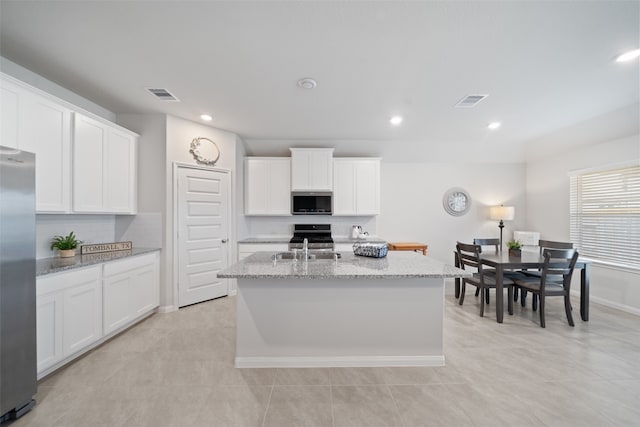 kitchen featuring light stone counters, a center island with sink, stainless steel appliances, decorative backsplash, and white cabinets