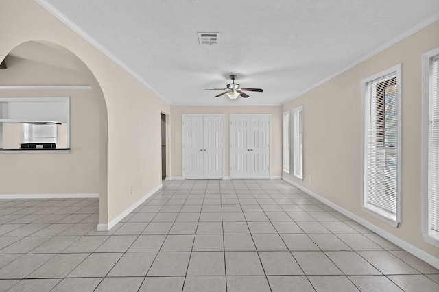 tiled empty room featuring ceiling fan, ornamental molding, and a textured ceiling