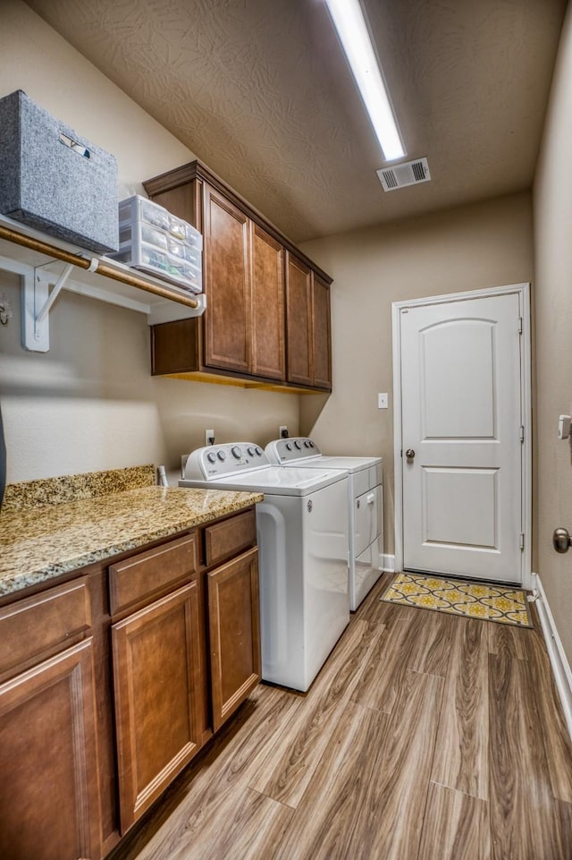 washroom with cabinets, washer and dryer, and light hardwood / wood-style flooring