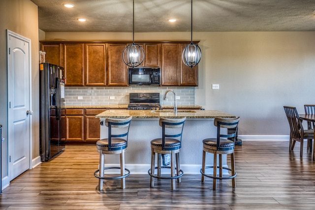 kitchen with sink, a kitchen island with sink, hanging light fixtures, black appliances, and a kitchen bar