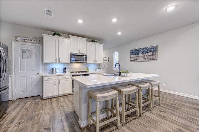 kitchen with appliances with stainless steel finishes, sink, a center island with sink, and white cabinets