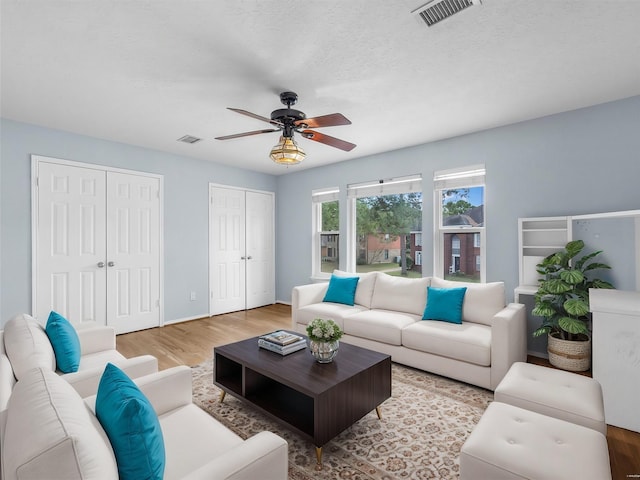 living room with ceiling fan, a textured ceiling, and light hardwood / wood-style floors