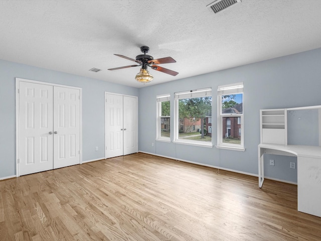 unfurnished bedroom featuring ceiling fan, a textured ceiling, light hardwood / wood-style flooring, and multiple closets