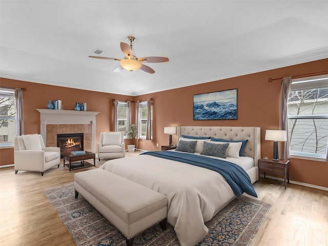 bedroom with crown molding, a fireplace, ceiling fan, and light wood-type flooring