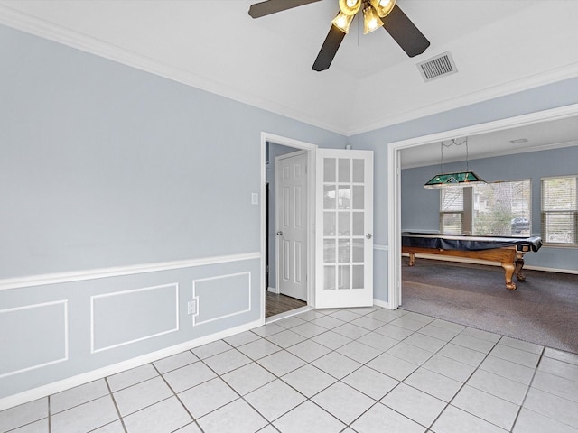 empty room featuring light tile patterned floors, visible vents, ornamental molding, wainscoting, and light carpet