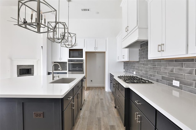 kitchen with stainless steel appliances, white cabinetry, sink, and a center island with sink