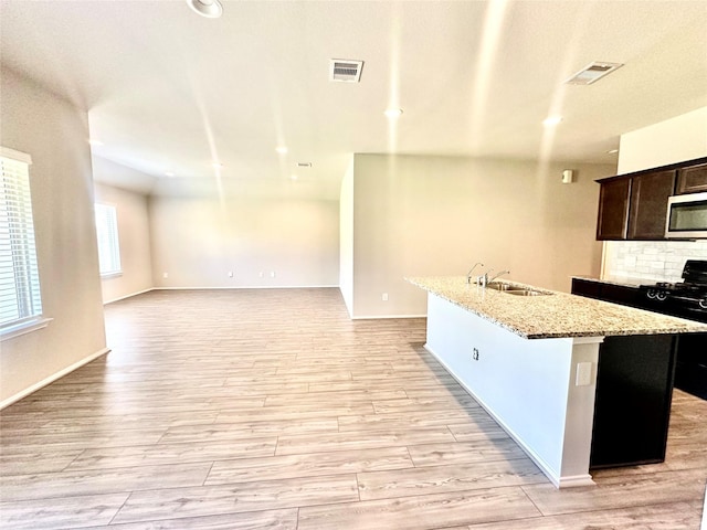 kitchen with sink, light hardwood / wood-style flooring, black range with gas stovetop, an island with sink, and backsplash