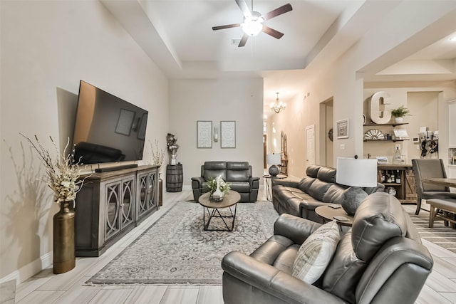 living room with ceiling fan with notable chandelier and a raised ceiling