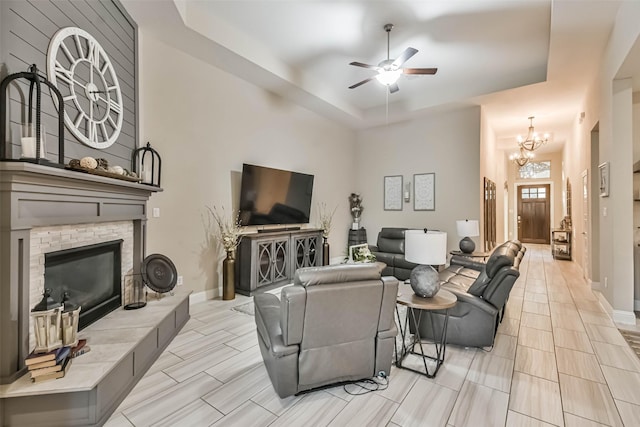 living room with a fireplace, a tray ceiling, and ceiling fan with notable chandelier