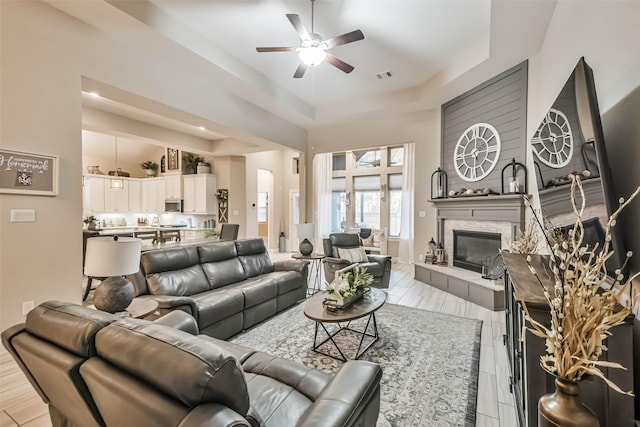 living room with a stone fireplace, a raised ceiling, ceiling fan, and a towering ceiling