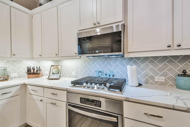 kitchen with tasteful backsplash, white cabinetry, appliances with stainless steel finishes, and light stone counters