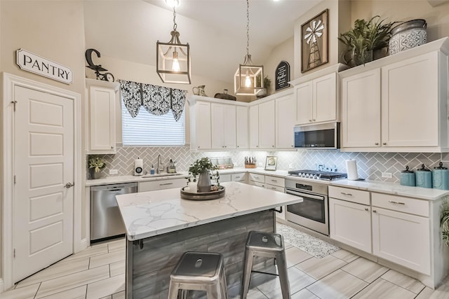 kitchen with a kitchen bar, white cabinetry, hanging light fixtures, a kitchen island, and stainless steel appliances