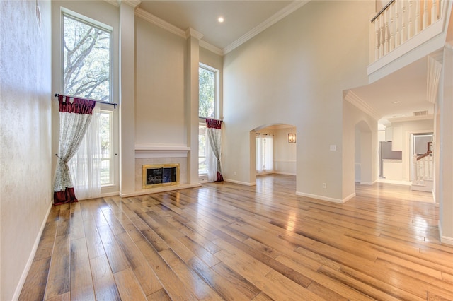 unfurnished living room with a high end fireplace, ornamental molding, light hardwood / wood-style floors, and a high ceiling