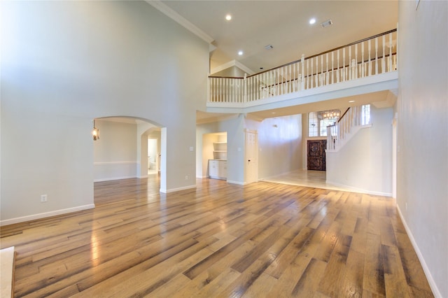 unfurnished living room with hardwood / wood-style floors, crown molding, and a high ceiling