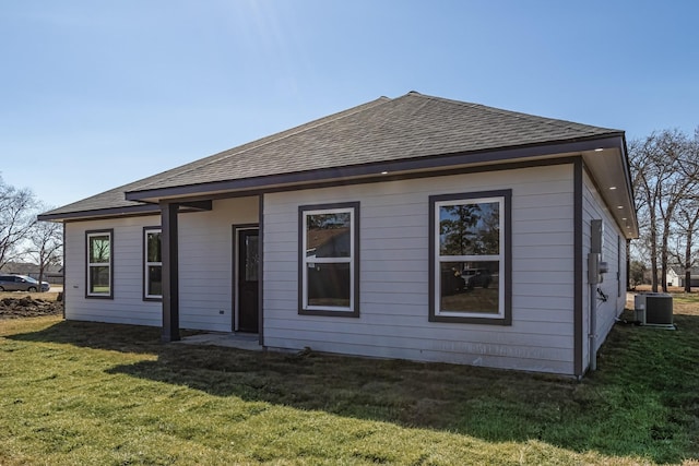 rear view of house with central AC and a lawn