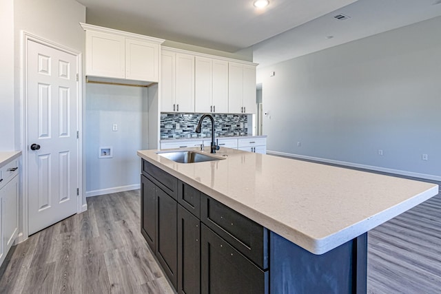 kitchen with backsplash, sink, a center island with sink, and white cabinets