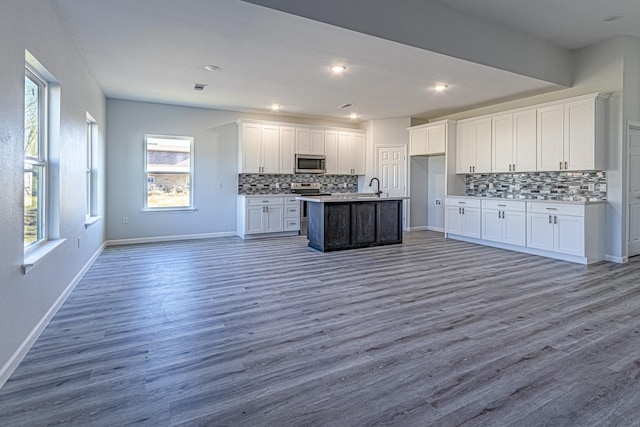 kitchen with sink, hardwood / wood-style flooring, stainless steel appliances, white cabinets, and a center island with sink