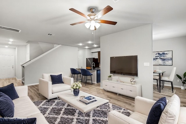 living room featuring light wood-type flooring, visible vents, baseboards, and a ceiling fan