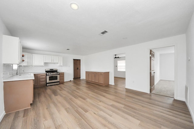 kitchen featuring sink, white cabinetry, stainless steel range, light hardwood / wood-style floors, and decorative backsplash