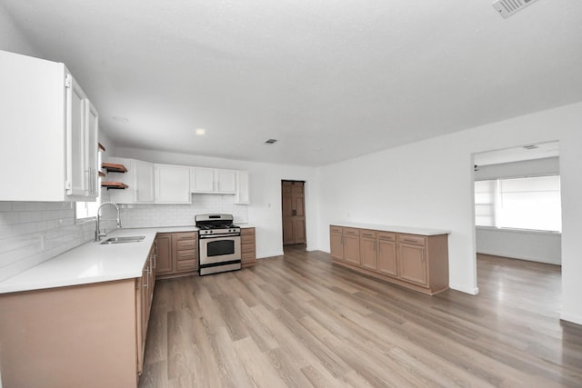 kitchen with sink, stainless steel gas range, white cabinetry, backsplash, and light hardwood / wood-style floors