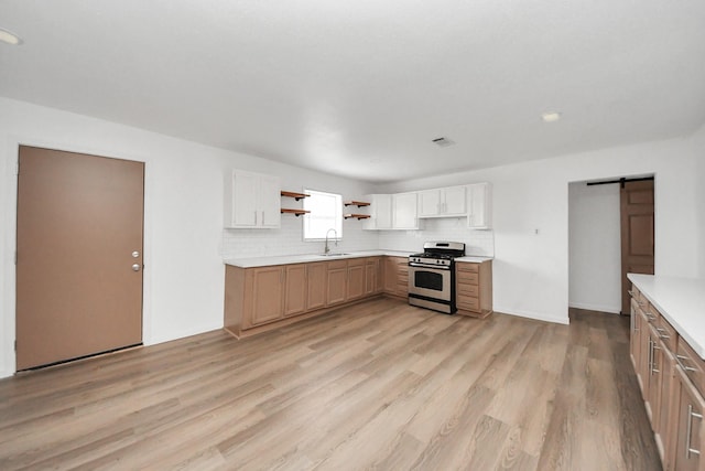 kitchen with sink, white cabinetry, decorative backsplash, stainless steel range with gas cooktop, and a barn door