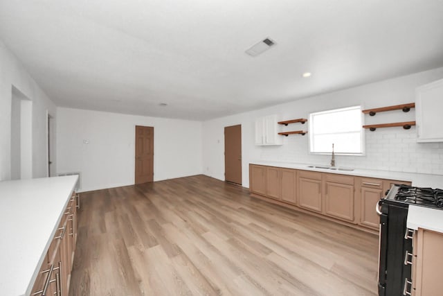 kitchen featuring sink, light hardwood / wood-style floors, gas range oven, white cabinets, and decorative backsplash