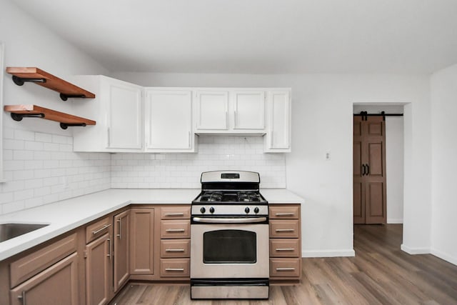 kitchen featuring a barn door, white cabinetry, stainless steel range with gas cooktop, and backsplash