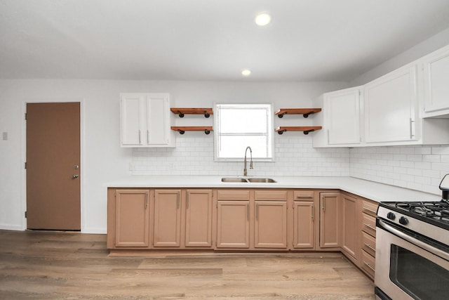 kitchen featuring sink, stainless steel gas range oven, light wood-type flooring, decorative backsplash, and white cabinets