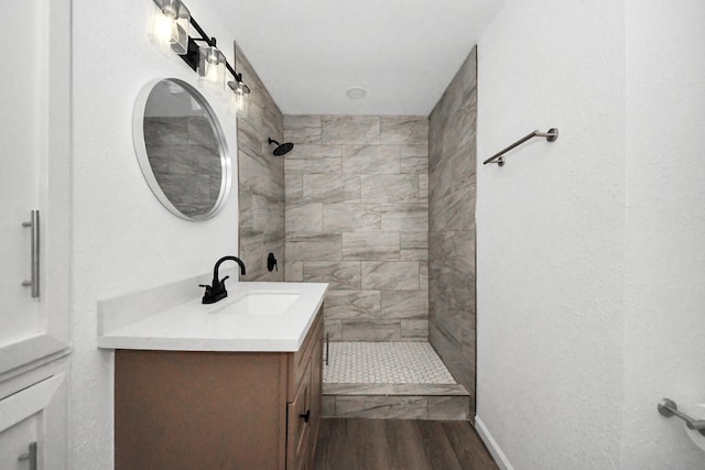 bathroom featuring a tile shower, vanity, and wood-type flooring