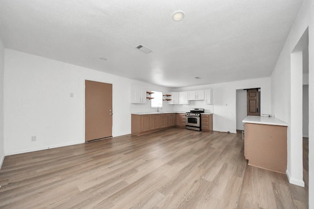 kitchen featuring sink, gas range, a textured ceiling, light wood-type flooring, and white cabinets